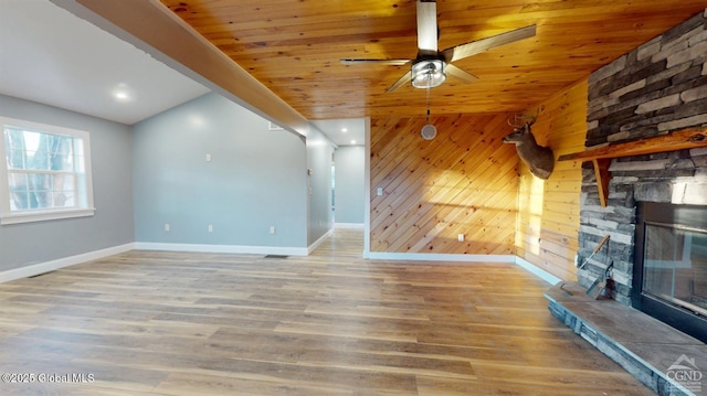 unfurnished living room featuring wooden walls, a stone fireplace, ceiling fan, and wood finished floors