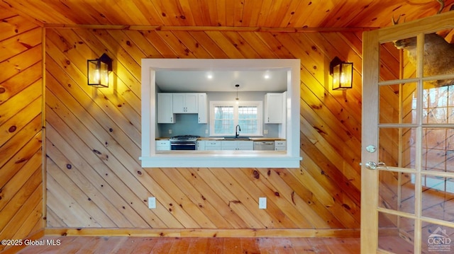 kitchen with wooden walls, a sink, wood ceiling, appliances with stainless steel finishes, and white cabinetry