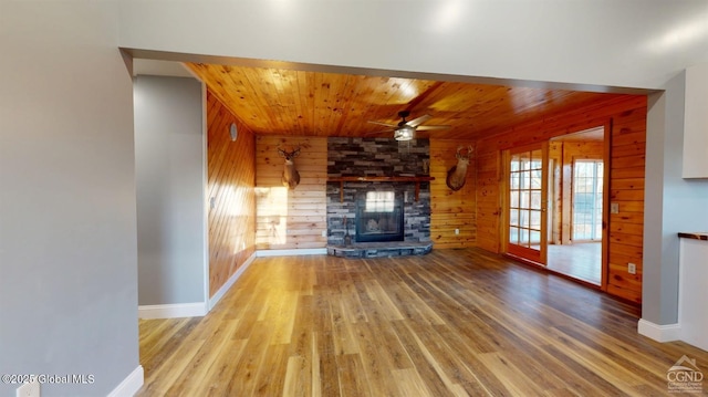 unfurnished living room with wood finished floors, wooden walls, a stone fireplace, wood ceiling, and ceiling fan