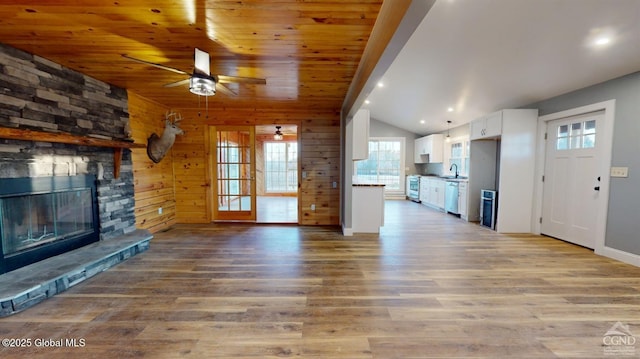 unfurnished living room with light wood-style flooring, wooden walls, a fireplace, and ceiling fan