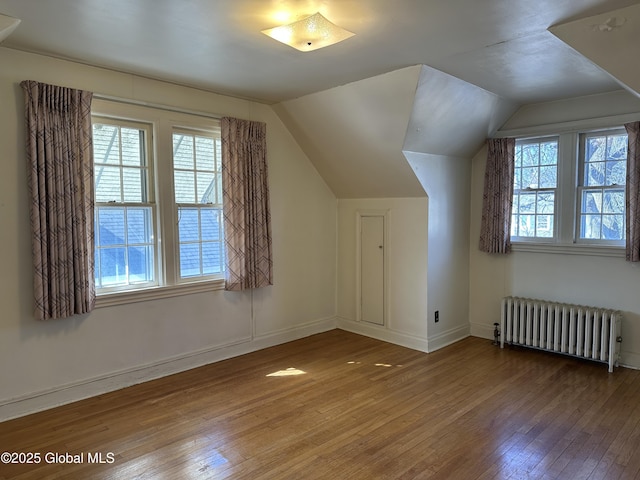 bonus room featuring radiator, a healthy amount of sunlight, vaulted ceiling, and hardwood / wood-style flooring