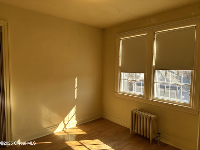 unfurnished room with baseboards, wood finished floors, and radiator heating unit