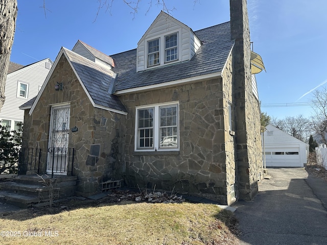 view of front of house featuring stone siding, a chimney, a detached garage, and an outdoor structure