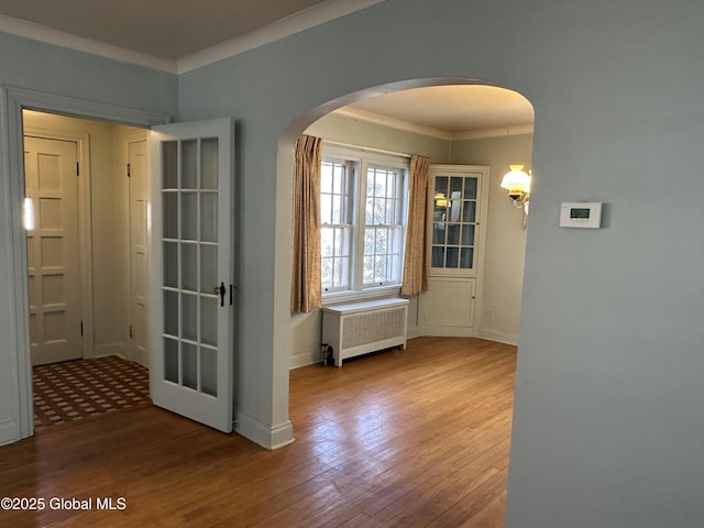 interior space featuring radiator, wood finished floors, baseboards, arched walkways, and ornamental molding