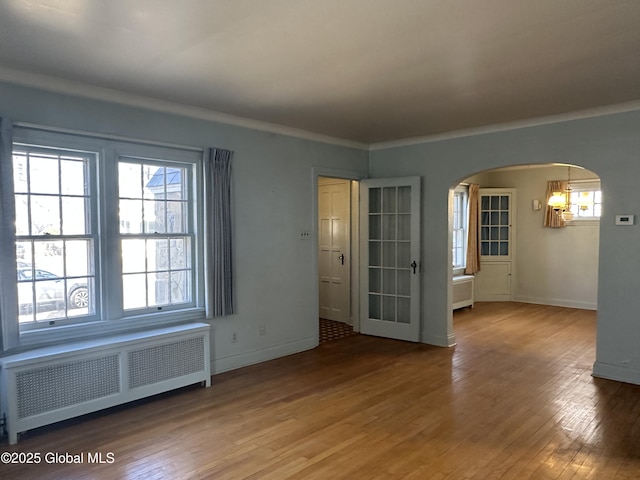 spare room with arched walkways, radiator, baseboards, and hardwood / wood-style flooring