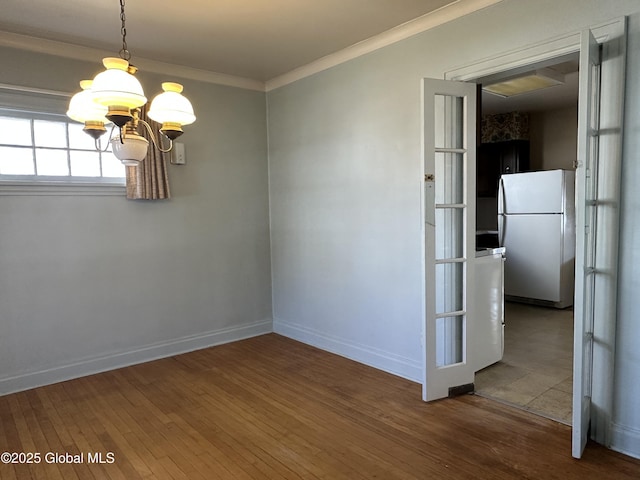 empty room with baseboards, crown molding, an inviting chandelier, and hardwood / wood-style floors