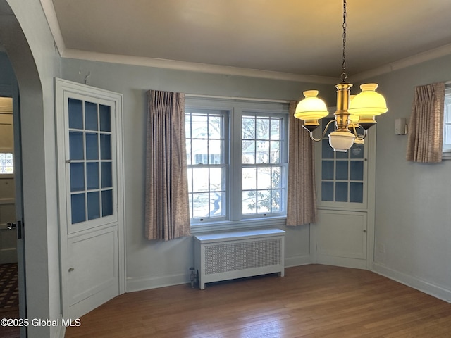 unfurnished dining area featuring radiator, baseboards, an inviting chandelier, wood finished floors, and arched walkways