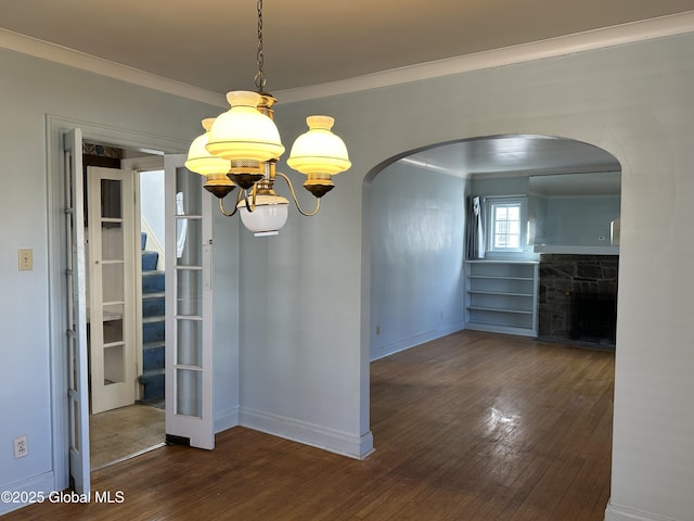 unfurnished dining area featuring wood finished floors, an inviting chandelier, a fireplace, arched walkways, and ornamental molding