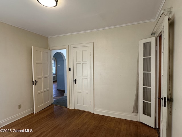 unfurnished room featuring arched walkways, crown molding, dark wood-type flooring, and baseboards