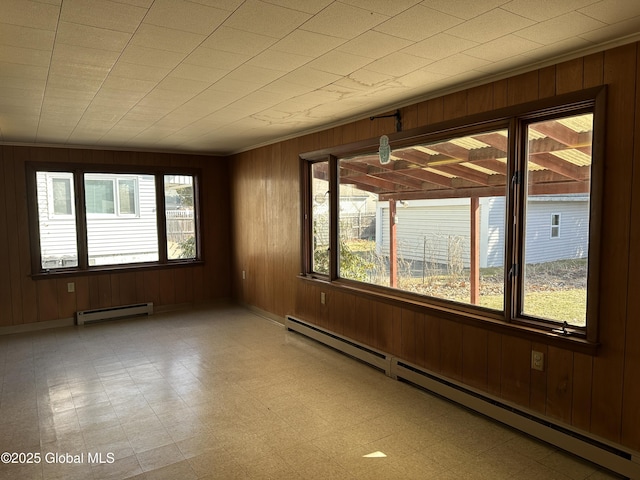 empty room featuring wooden walls, light floors, a baseboard heating unit, and a baseboard radiator