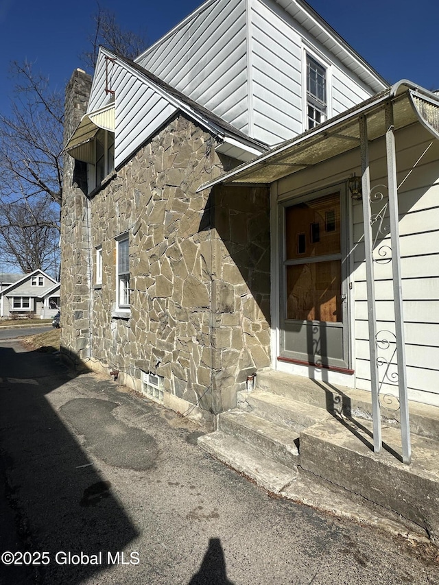 entrance to property featuring stone siding and a chimney