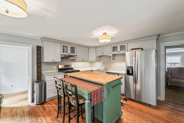 kitchen with under cabinet range hood, a sink, stainless steel appliances, decorative backsplash, and wooden counters