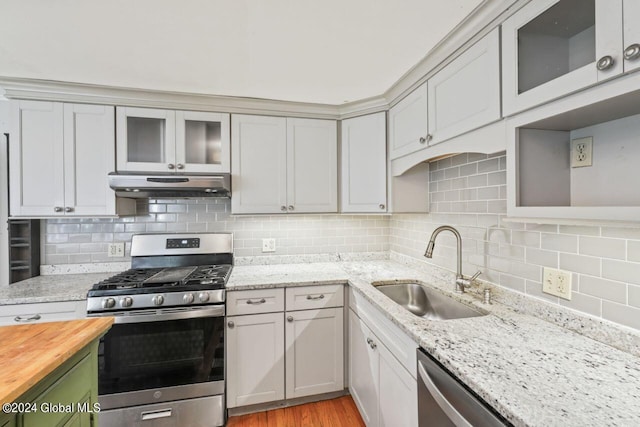 kitchen with under cabinet range hood, decorative backsplash, gas range, and a sink