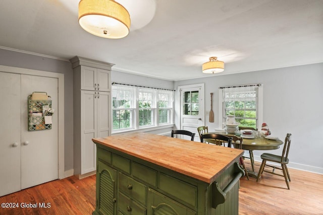 kitchen featuring baseboards, wooden counters, green cabinetry, crown molding, and light wood-type flooring