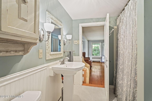 bathroom featuring toilet, radiator heating unit, and a wainscoted wall