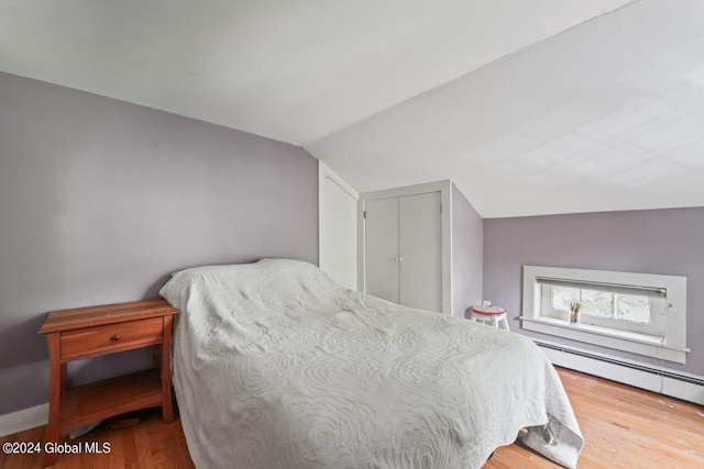 bedroom with wood finished floors, lofted ceiling, and a baseboard radiator