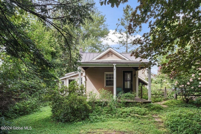 view of home's exterior featuring a standing seam roof, a porch, a chimney, and metal roof