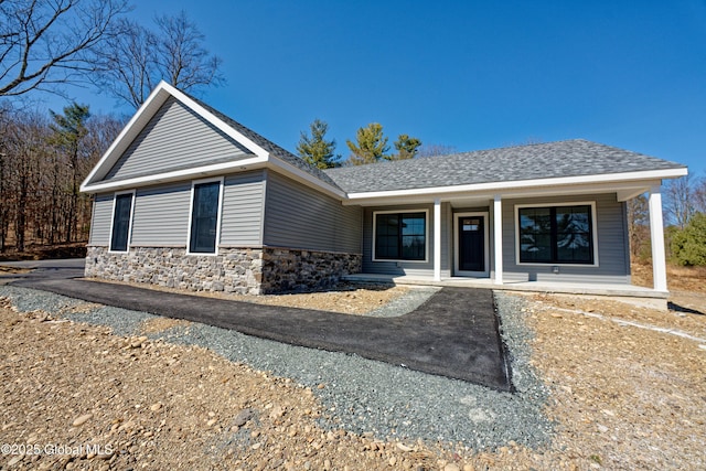 view of front of house with a porch, stone siding, and roof with shingles