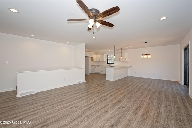 unfurnished living room featuring wood finished floors, visible vents, baseboards, recessed lighting, and ceiling fan with notable chandelier