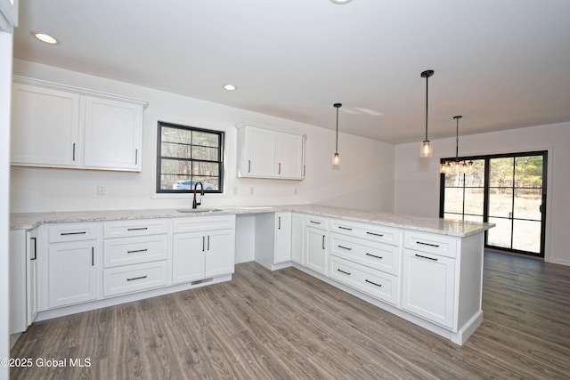 kitchen with white cabinetry, a peninsula, wood finished floors, and a sink