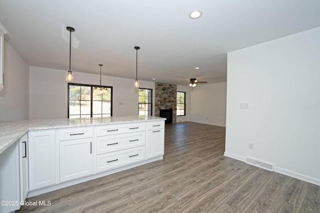 kitchen with visible vents, light wood-style floors, a stone fireplace, white cabinets, and ceiling fan