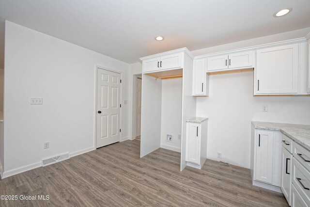 kitchen with light stone counters, visible vents, wood finished floors, and white cabinetry