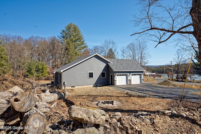 view of side of property featuring an attached garage, roof with shingles, and driveway