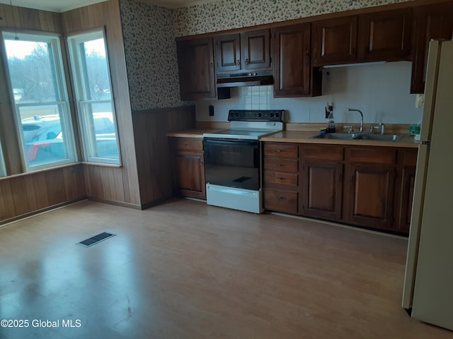 kitchen featuring light countertops, freestanding refrigerator, electric range oven, wainscoting, and under cabinet range hood