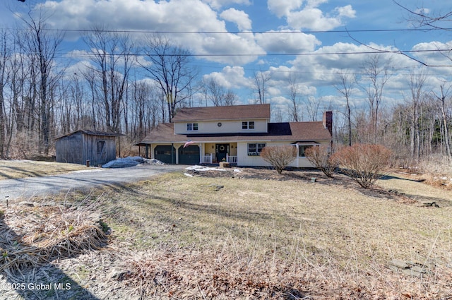 view of front of property featuring an outbuilding, driveway, covered porch, a chimney, and a garage