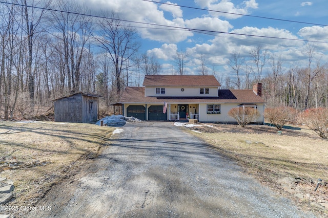 view of front of house with driveway, covered porch, an outdoor structure, a garage, and a chimney