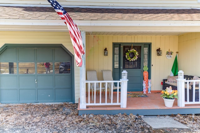 doorway to property featuring a garage, covered porch, and roof with shingles