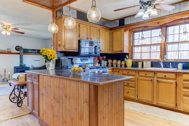 kitchen featuring stainless steel gas range oven, ceiling fan, black microwave, a wood stove, and a sink