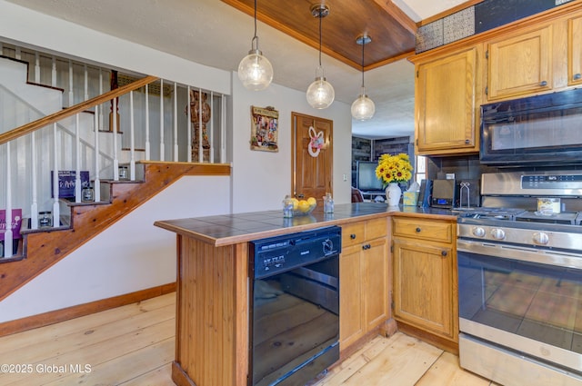 kitchen featuring tile countertops, a peninsula, black appliances, decorative light fixtures, and light wood-type flooring