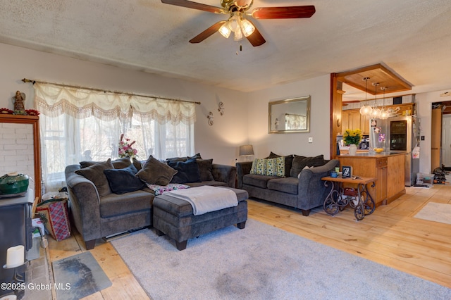 living room featuring light wood-style flooring, ceiling fan with notable chandelier, and a textured ceiling