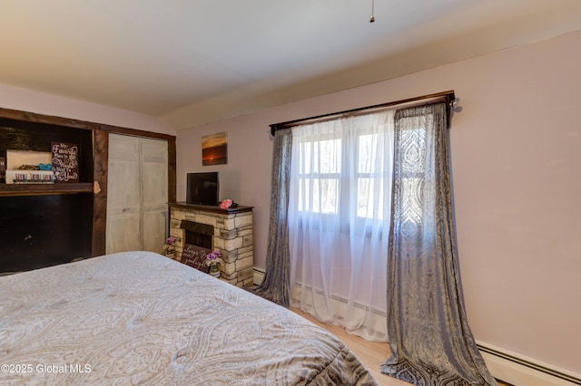 bedroom featuring wood finished floors, a fireplace, a closet, and baseboard heating