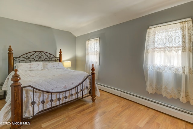 bedroom with a baseboard radiator, multiple windows, wood finished floors, and vaulted ceiling