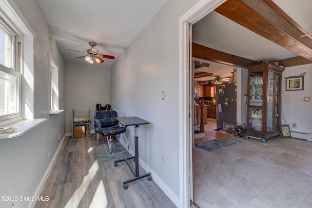 office featuring wood finished floors, beamed ceiling, ceiling fan with notable chandelier, and baseboards