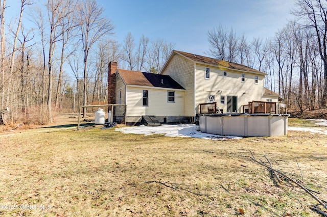 back of property featuring a covered pool, a wooden deck, a yard, and a chimney