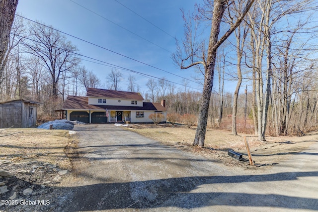 view of front of house featuring aphalt driveway, covered porch, an attached garage, and a chimney