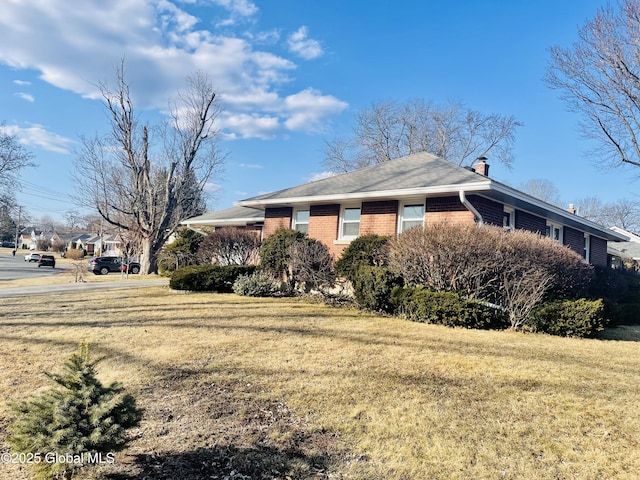 view of side of home featuring brick siding, a lawn, and a chimney