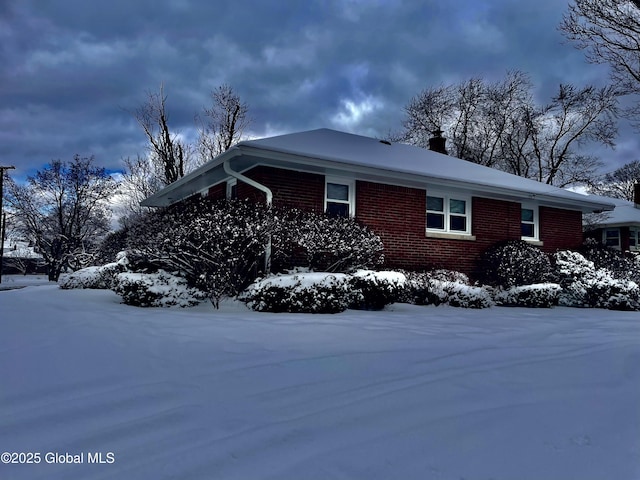 snow covered property with brick siding and a chimney