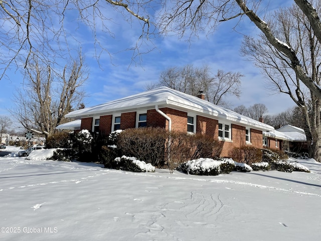 view of snow covered exterior featuring brick siding and a chimney