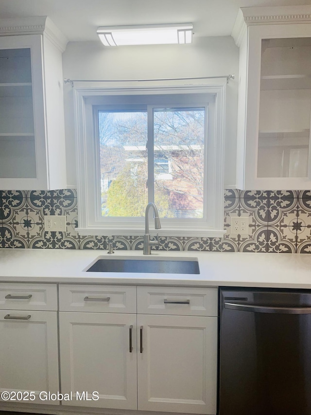 kitchen with a sink, tasteful backsplash, white cabinetry, light countertops, and dishwashing machine