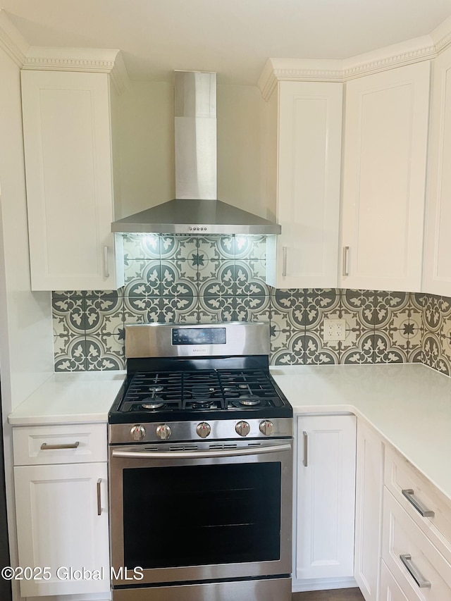 kitchen with stainless steel gas range oven, backsplash, wall chimney range hood, light countertops, and white cabinets