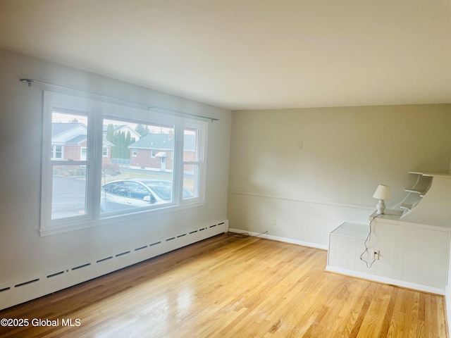 empty room featuring wainscoting, a baseboard heating unit, and wood finished floors