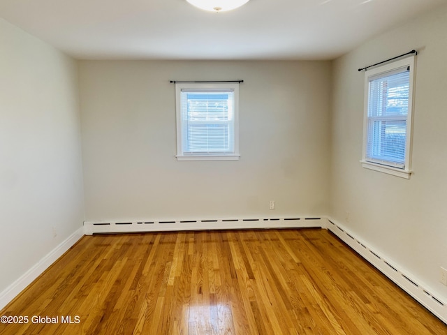 unfurnished room with a baseboard heating unit, wood finished floors, a healthy amount of sunlight, and baseboards