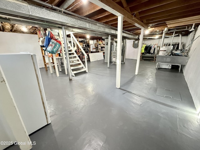 unfinished basement featuring heating unit, stairway, electric panel, and freestanding refrigerator