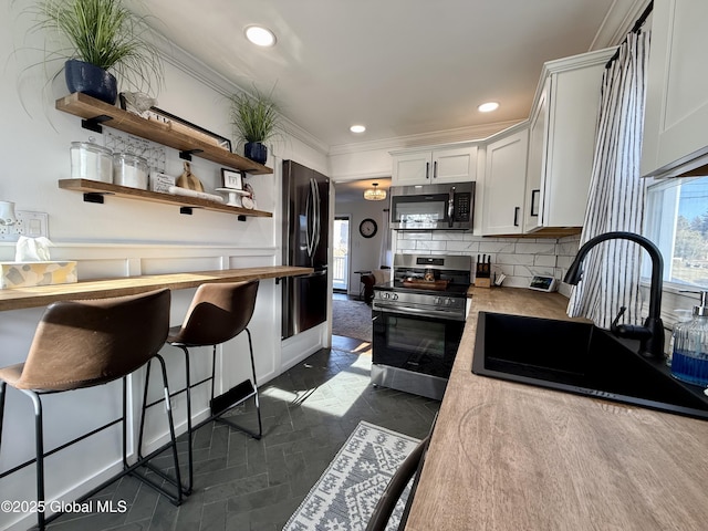 kitchen featuring a sink, backsplash, appliances with stainless steel finishes, white cabinets, and crown molding