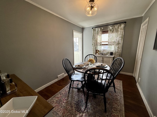 dining space with dark wood-type flooring, baseboards, visible vents, and ornamental molding