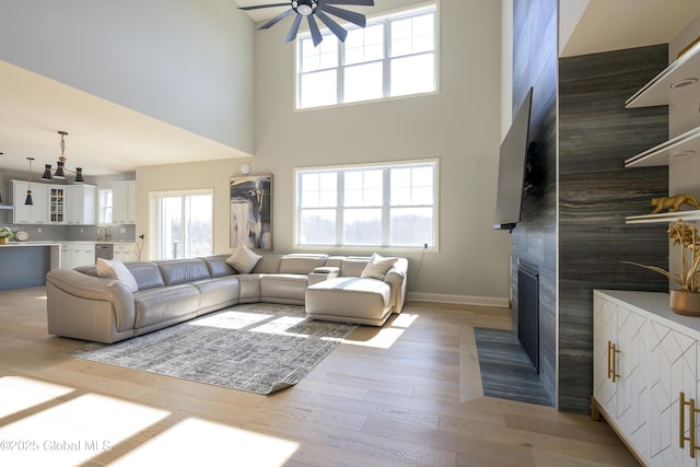 living area with wood finished floors, a ceiling fan, baseboards, a high ceiling, and a fireplace